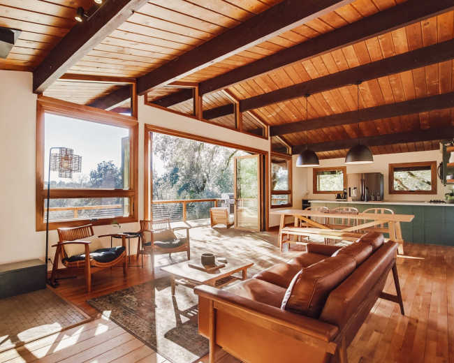A modern, open-concept living space with a wood-burning stove, large windows, and a dining area leading to a deck.