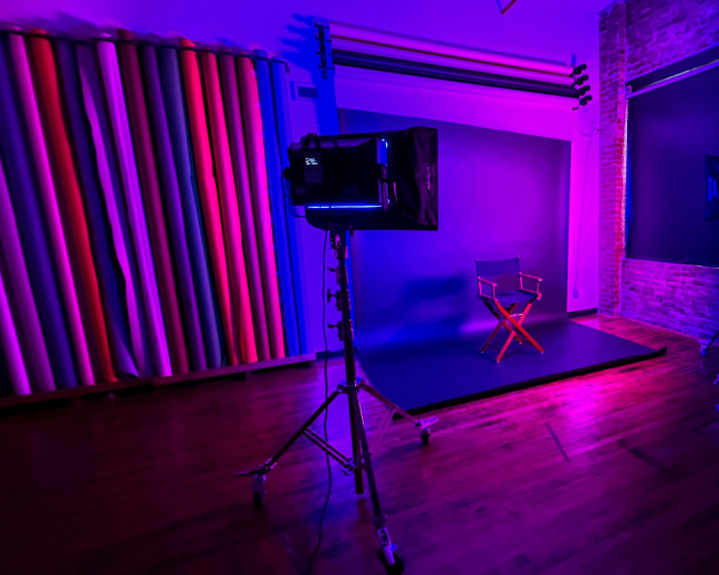 A photo studio is equipped with three lights illuminating a backdrop and an empty chair in a purple-tinted room.