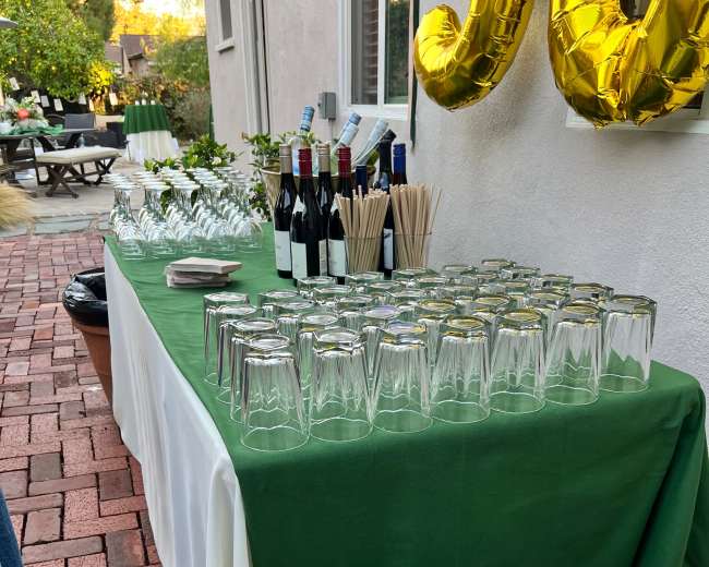 A table set with glasses, wine bottles, and drink straws is positioned beside a bin overflowing with empty beverage containers.