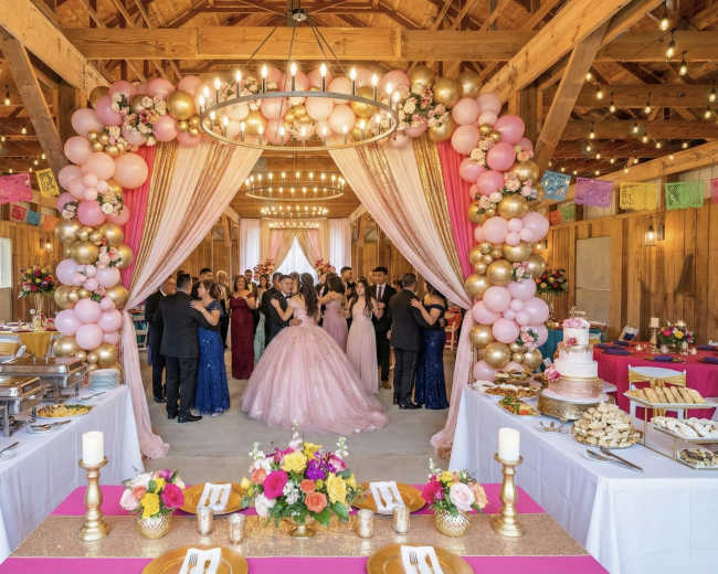 The image depicts a festive indoor event space decorated with balloons and floral arrangements, where guests are gathered in formal attire, celebrating a special occasion.