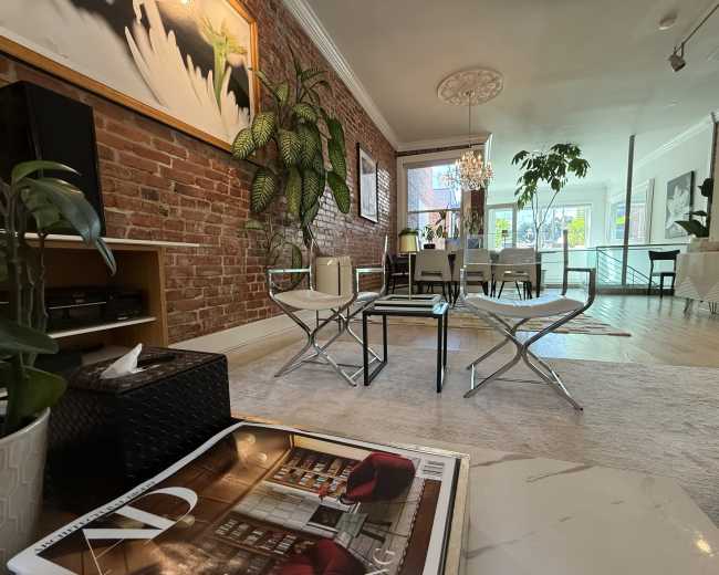 The image showcases a stylish living space featuring exposed brick walls, modern furnishings, a chandelier, and various plants.
