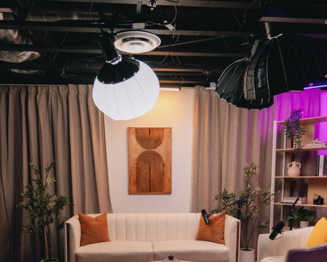 The image shows a cozy living room setup with a white sofa, a round wooden coffee table, and decorative plants, all under soft lighting and draped curtains.
