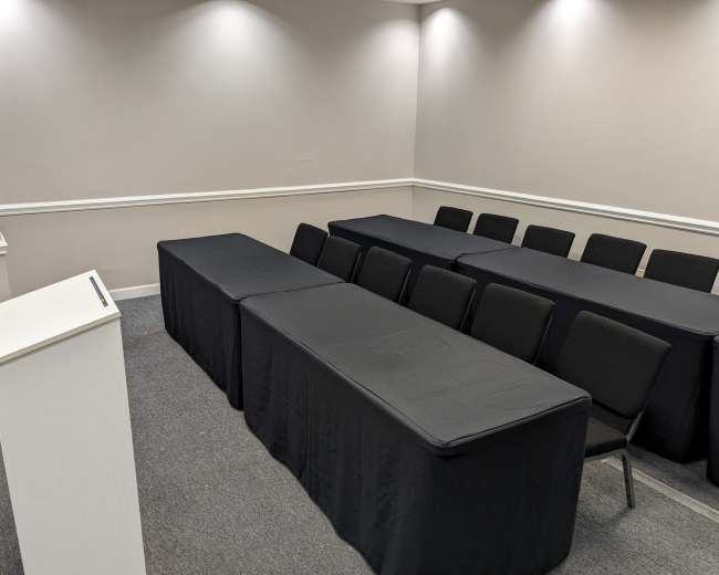 A conference room is set up with several rows of chairs facing a podium and tables covered in black cloth.