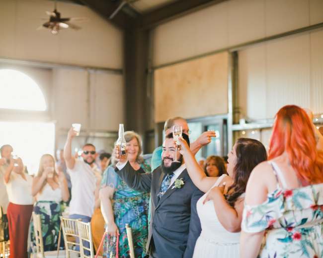A group of guests raises their glasses in a toast during a celebration at a spacious venue with large windows.