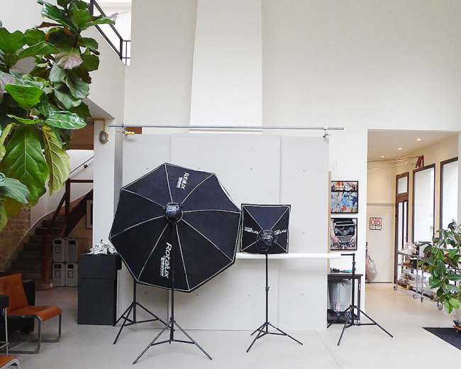 A well-lit studio space featuring two large softbox lights, a backdrop setup, and indoor plants.