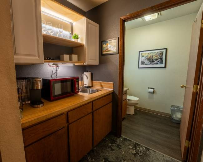 A small kitchenette with a microwave, coffee maker, and a bathroom entrance in a compact space.
