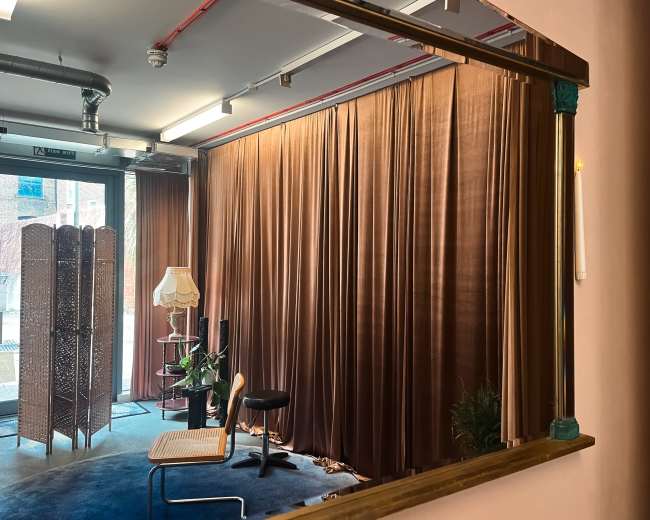The image shows a room with brown curtains, a chair, a lamp, and a plant, viewed from a mirrored perspective.