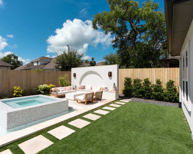 A landscaped backyard features a concrete seating area, a small plunge pool, and a well-maintained lawn bordered by a wooden fence.