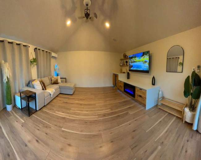 The image shows a modern living room featuring a gray sectional sofa, a TV mounted on the wall, and wooden flooring with minimal decorative elements.