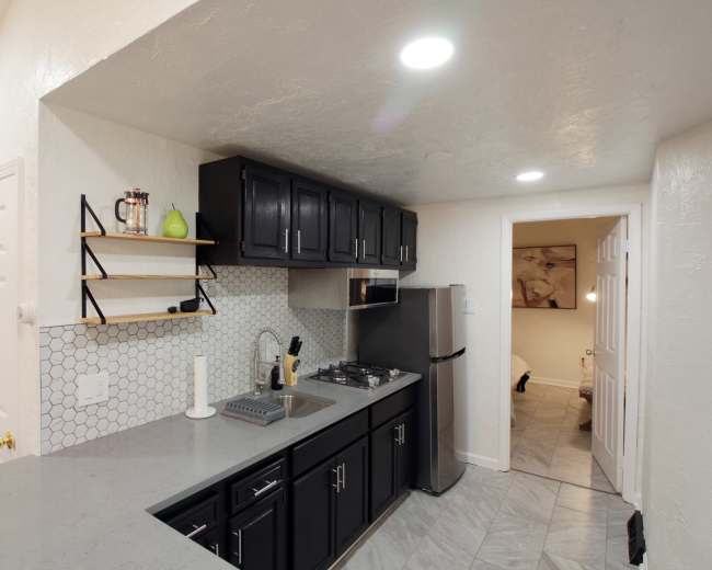A modern kitchen featuring dark cabinetry, a gray countertop, and a hexagonal tile backsplash, with a doorway leading to another room in the background.