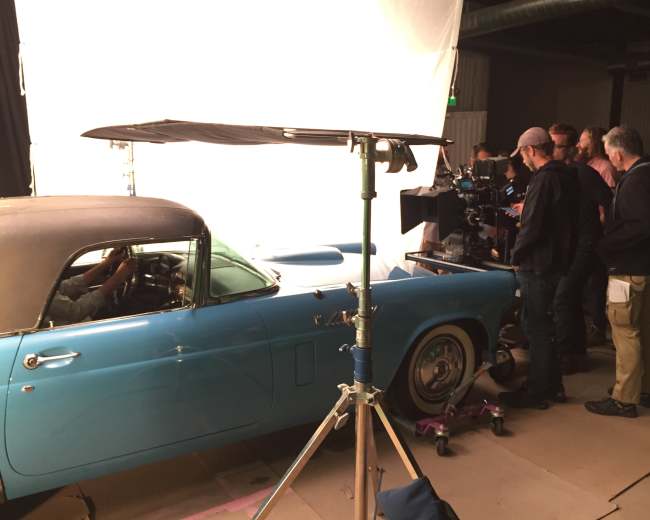 The image shows a studio space with a gradient backdrop of vibrant colors including purple, blue, and green.