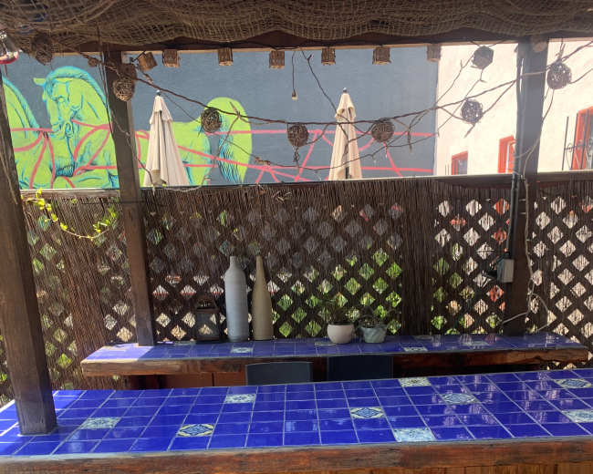 An outdoor bar area with a blue tiled countertop, wooden structure, and two metal chairs.