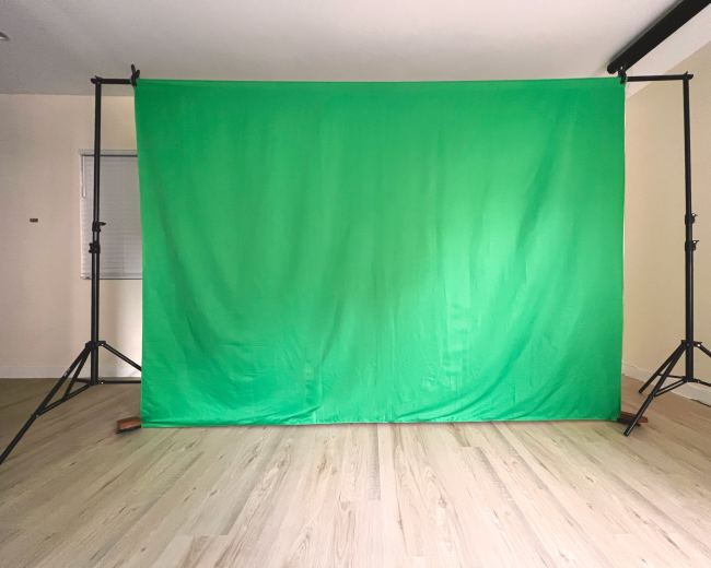 A green backdrop is set up on stands in a minimalist room with light wooden flooring.