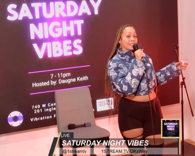 A performer stands on stage holding a microphone, with a large sign reading "SATURDAY NIGHT VIBES" in the background.