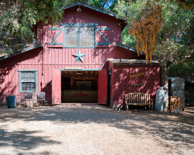 A red barn with a green star on the front is situated among trees, with a gravel path leading to it.
