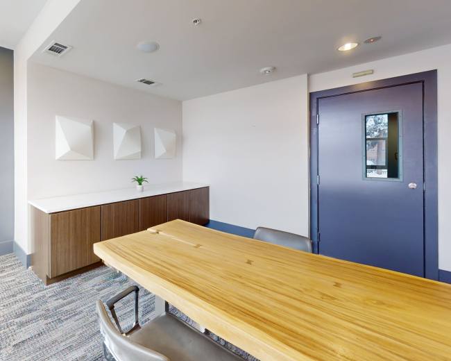 The image shows a modern conference room with a wood table, gray walls, and a minimalistic design.