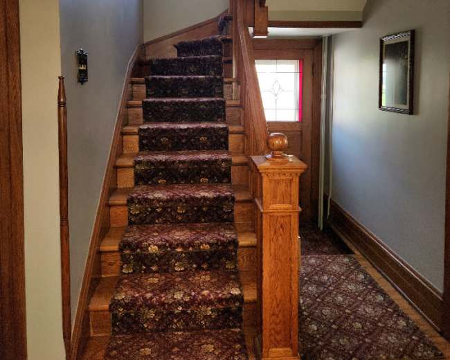 The image shows a staircase with a carpet runner leading up to a window, along with a hallway visible at the top.