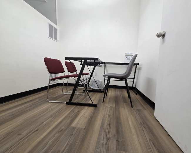 The image shows a small room with a table, four chairs, and a wastebasket on a wooden floor.