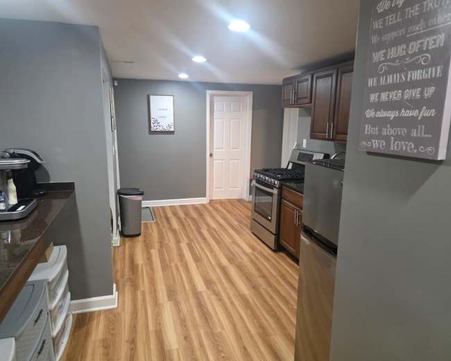 The image shows a modern kitchen with wood-finished flooring, stainless steel appliances, and gray walls.