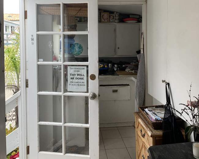 A small entryway with a glass-paned door leading to a kitchenette, featuring a table and various kitchen items visible on the counter.