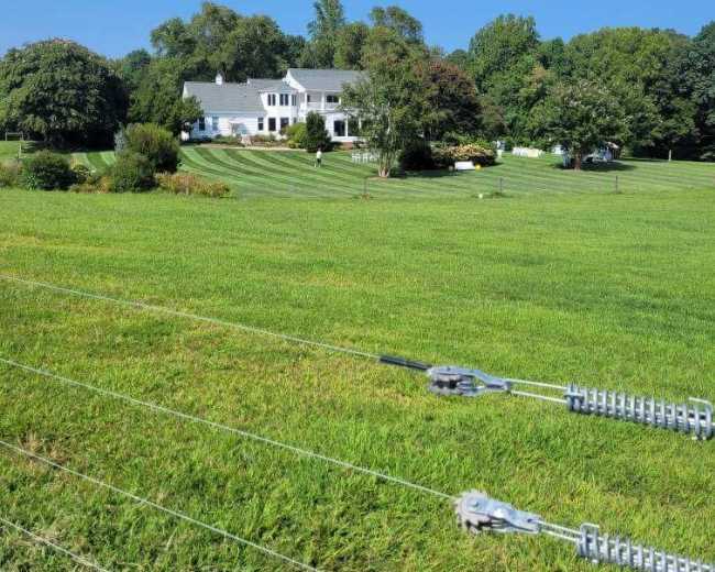 A large, white house sits in the background of a green, grassy field under a clear blue sky.