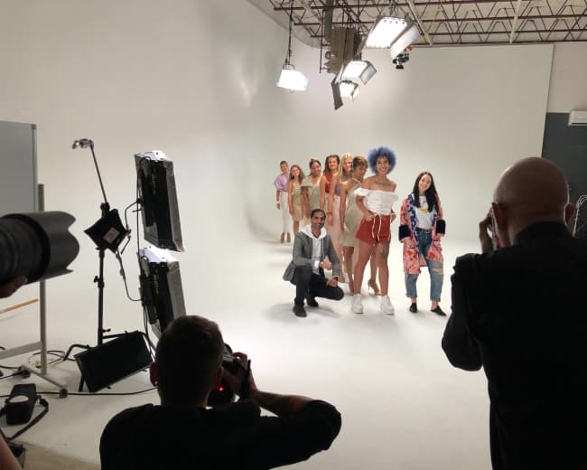 A group of models poses for a photo shoot in a studio with bright lighting and a seamless white backdrop.