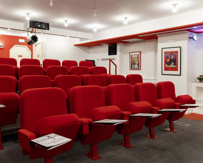 A small red theater with empty rows of plush seats and posters on the walls.