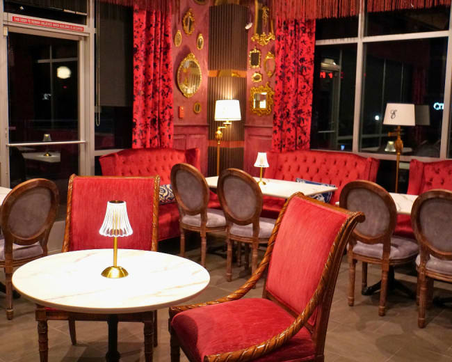 The interior of a stylish cafe features red velvet seating, marble tables, and decorative mirrors on the walls.