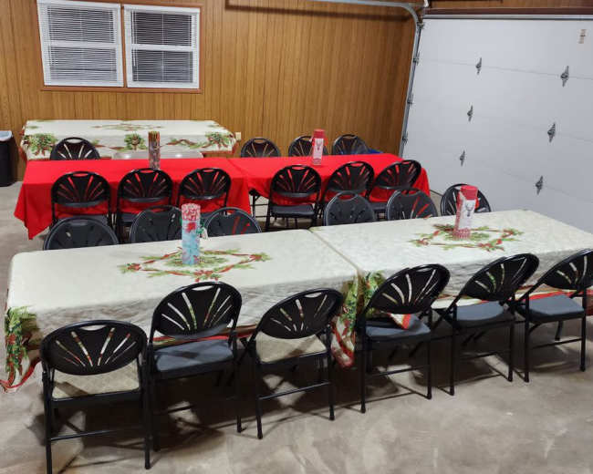A garage with several tables covered in holiday-themed tablecloths arranged in rows, accompanied by a dog on the floor.