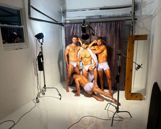 A group of four male models poses in a studio setting with bright lighting and a glossy white floor.