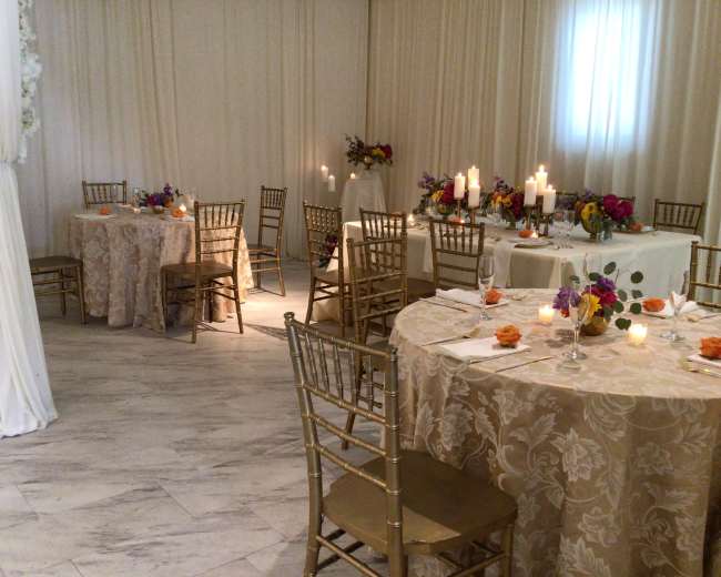 A decorated event space with several round tables covered in patterned tablecloths, each set with floral centerpieces and candles.
