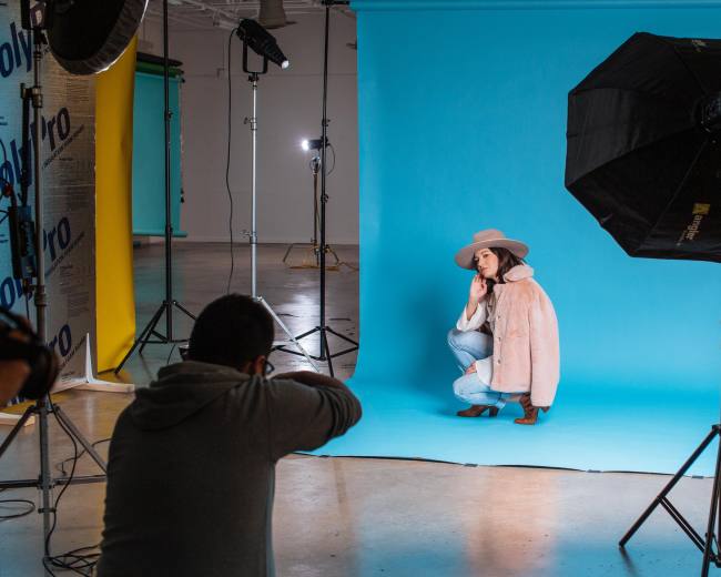 A photographer captures a model posing in front of a turquoise backdrop in a studio setting with various lighting equipment.