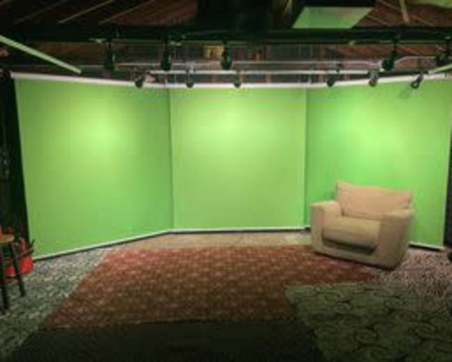 A room with three green screens arranged in a corner and a beige couch placed on a patterned rug.