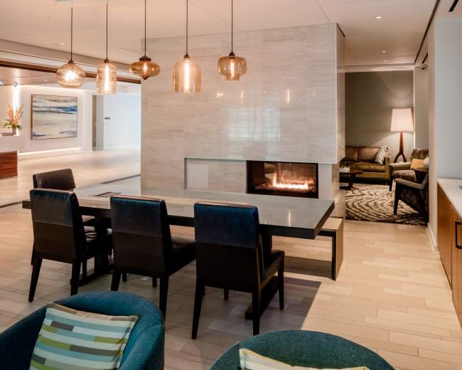 The image shows a modern lounge area with a fireplace, a dining table, and stylish seating arrangements, accented by pendant lights and a television.