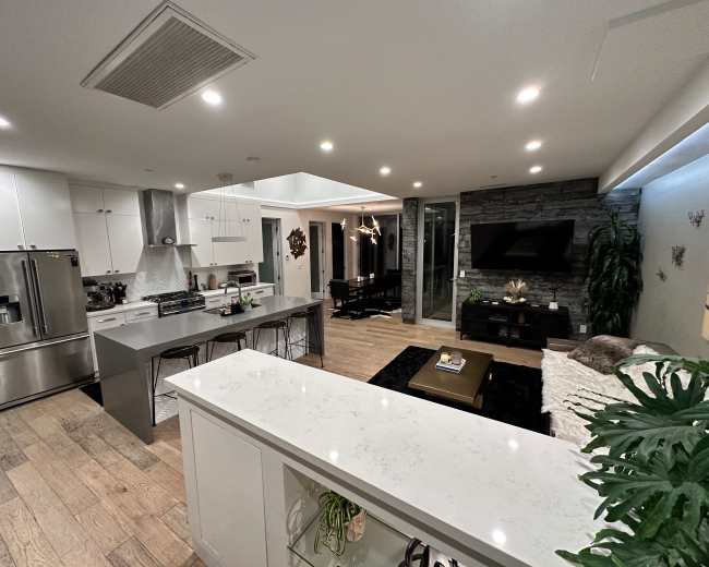 A modern open-concept kitchen and living area with white cabinetry, a stone accent wall, and dining space.