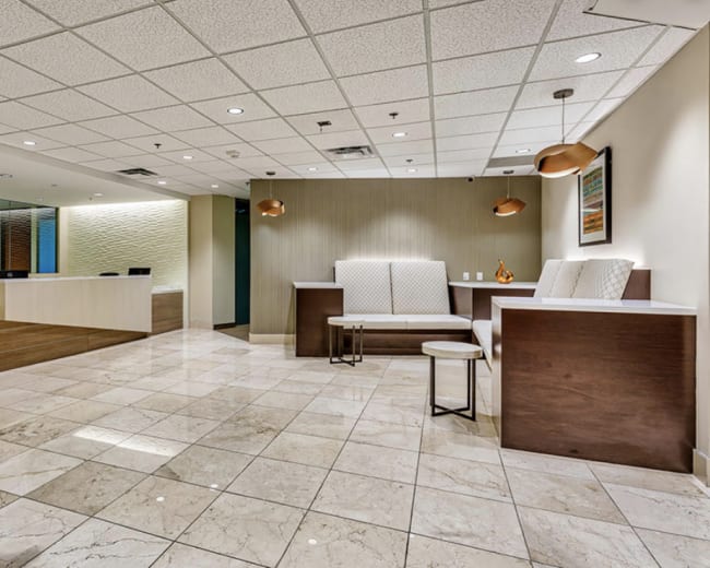A modern reception area with tiled flooring, a large front desk, and seating arrangements against the walls.