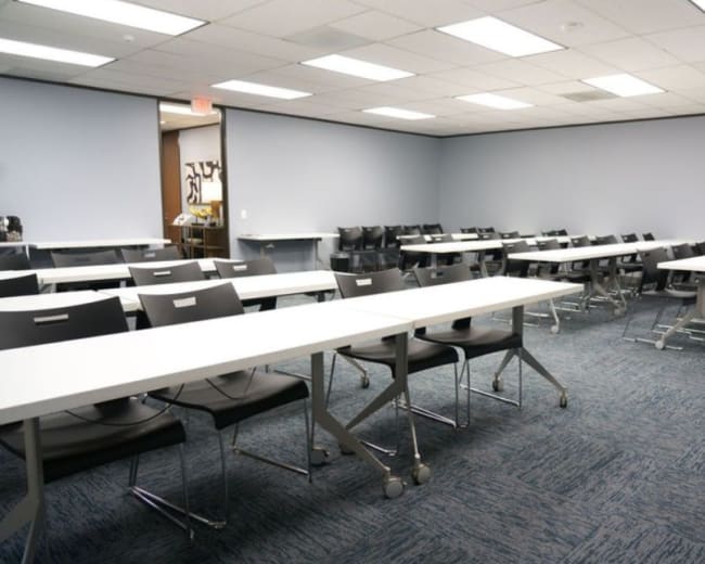 The image shows a classroom setup with several rows of tables and chairs arranged in a spacious, organized layout.