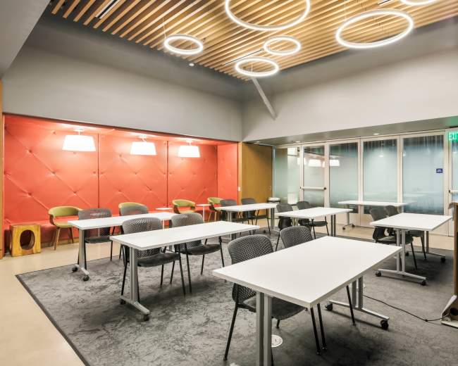 The image shows a modern meeting room with several tables arranged in a U-shape, backed by a red wall with soft lighting.