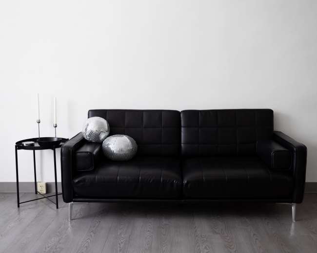 A black leather sofa with two disco balls on the seat sits next to a small, round table with two candles.
