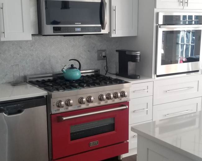 The image shows a modern kitchen featuring white cabinetry, stainless steel appliances, and a red gas stove.