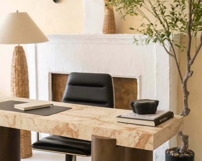 The image features a modern home office setup with a marble desk, a black chair, a lamp, and decorative plants near a fireplace.