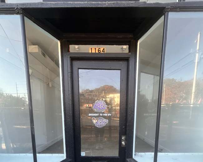 The image shows a black door with a glass storefront on either side, situated at the corner of a building.