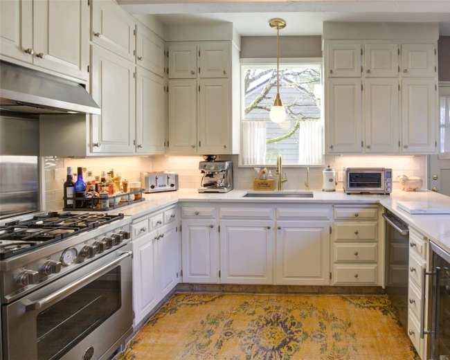 A modern kitchen with white cabinetry, stainless steel appliances, and a central island with a light-colored countertop.