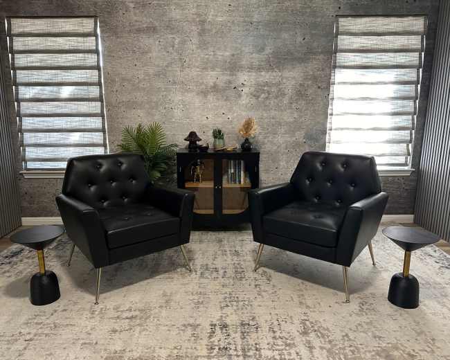 The scene features two black leather armchairs facing each other on a light-colored rug, with a dark wooden cabinet and decorative items in the background.