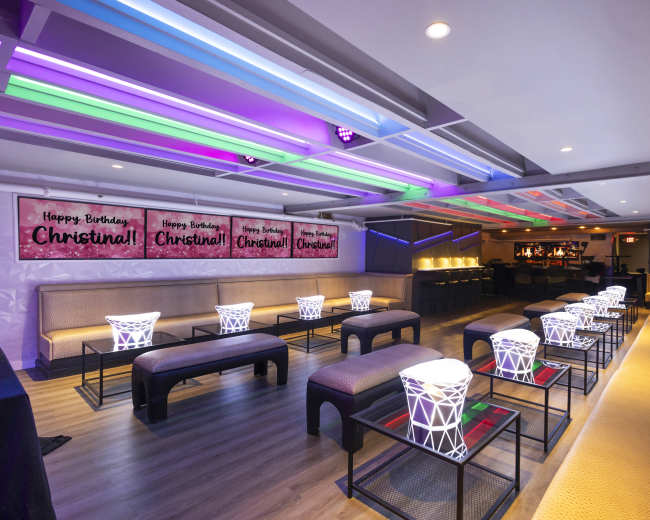 The image shows a vibrant birthday celebration venue decorated with colorful lights and banners that read "Happy Birthday, Christina!"