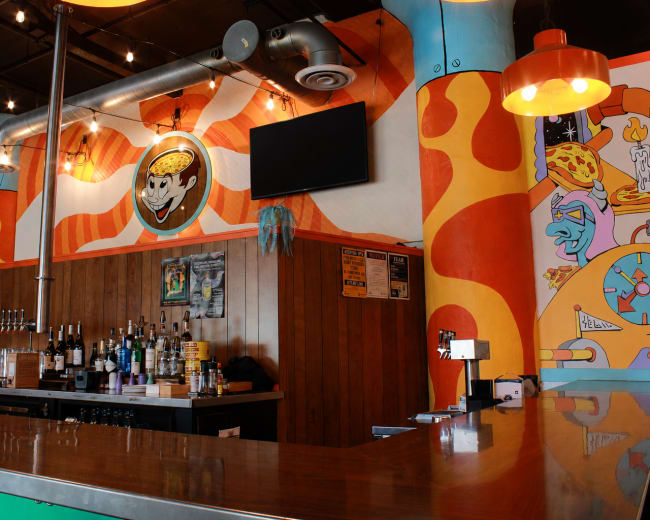 The image shows a vibrant bar area with colorful mural art on the walls and a polished wooden counter.
