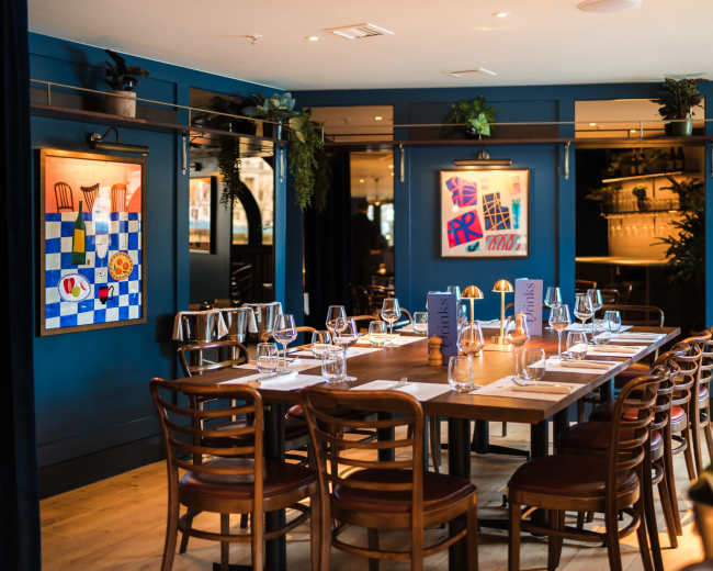 The image shows a neatly arranged dining table in a restaurant with blue walls adorned with framed artwork.
