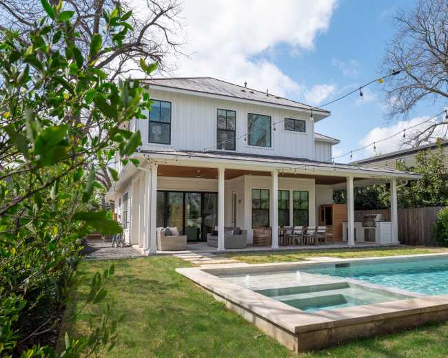 A two-story white house with a spacious backyard features a swimming pool and an outdoor dining area.