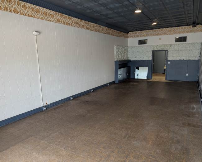 The image shows an empty room with a patterned wallpaper at the top, a wooden floor, and a single light fixture on the wall.