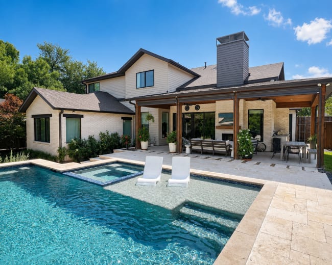 A modern two-story house with a swimming pool and a covered patio featuring outdoor furniture and landscaping around the property.